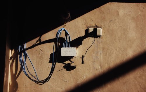 pexels photo 7400884 7400884 Electric blue wires connected to network adapter plugged in socket on shabby brown wall of building on street with shadow